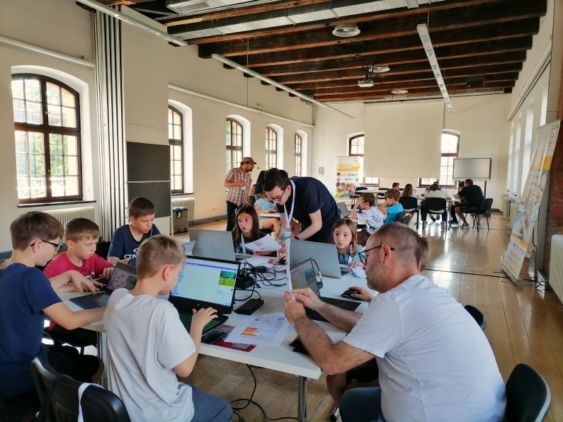Viele Kinder mit den Mentoren:innen am Programmieren